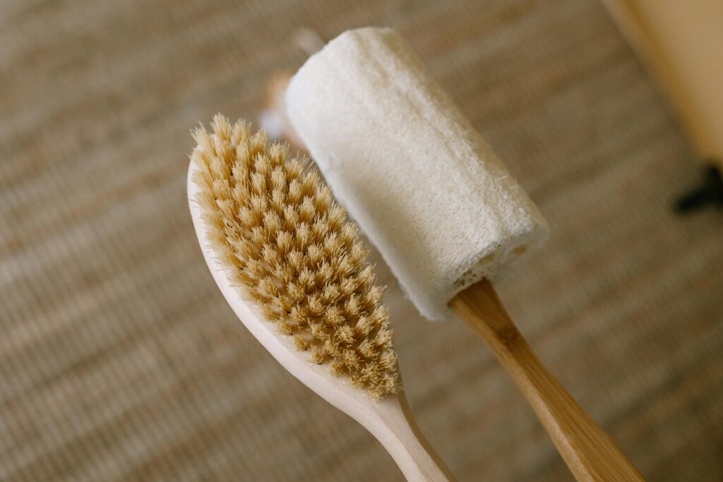 A detailed close-up of a natural wooden body brush and loofah on a textured surface.